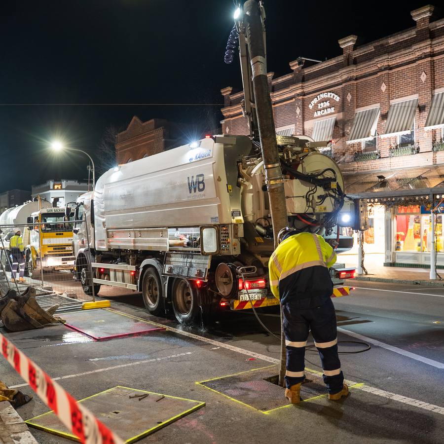 A WB vacuum truck and crew on a closed street at night.