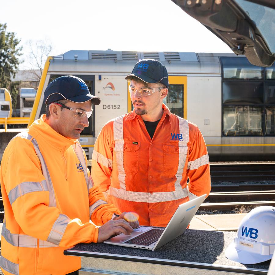 Two WB crew going over a job on a laptop beside the rail line.