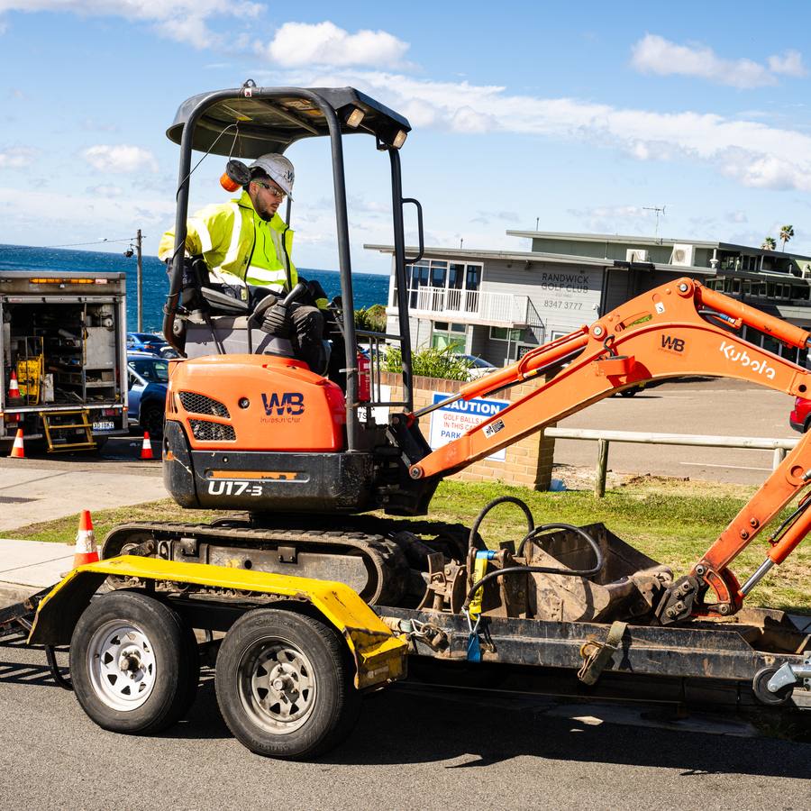 A mini excavator unloaded from a WB truck by the coast.