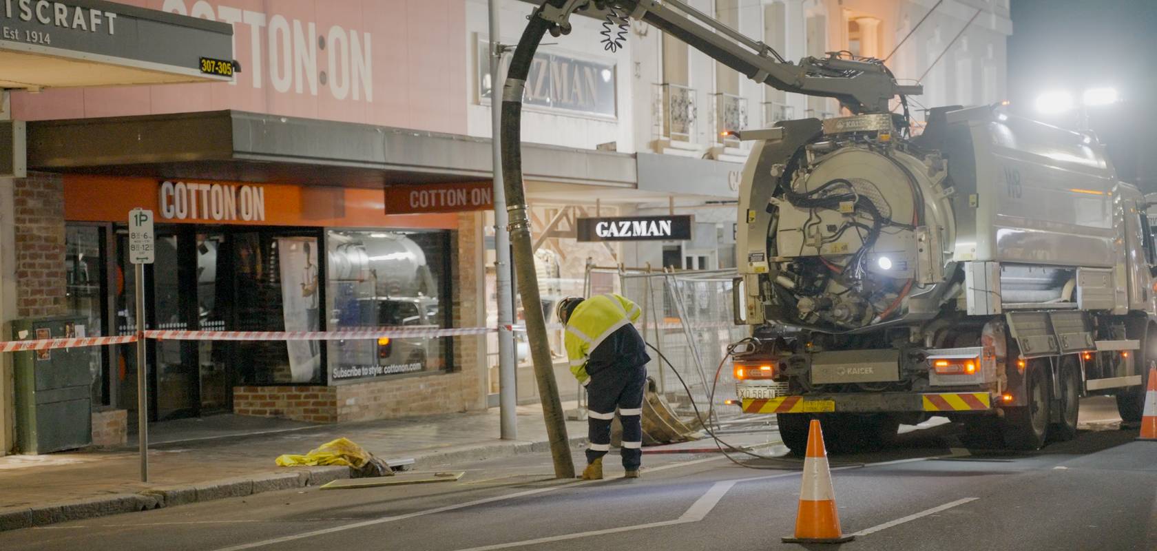 A WB vacuum truck working on a shopping strip at night.