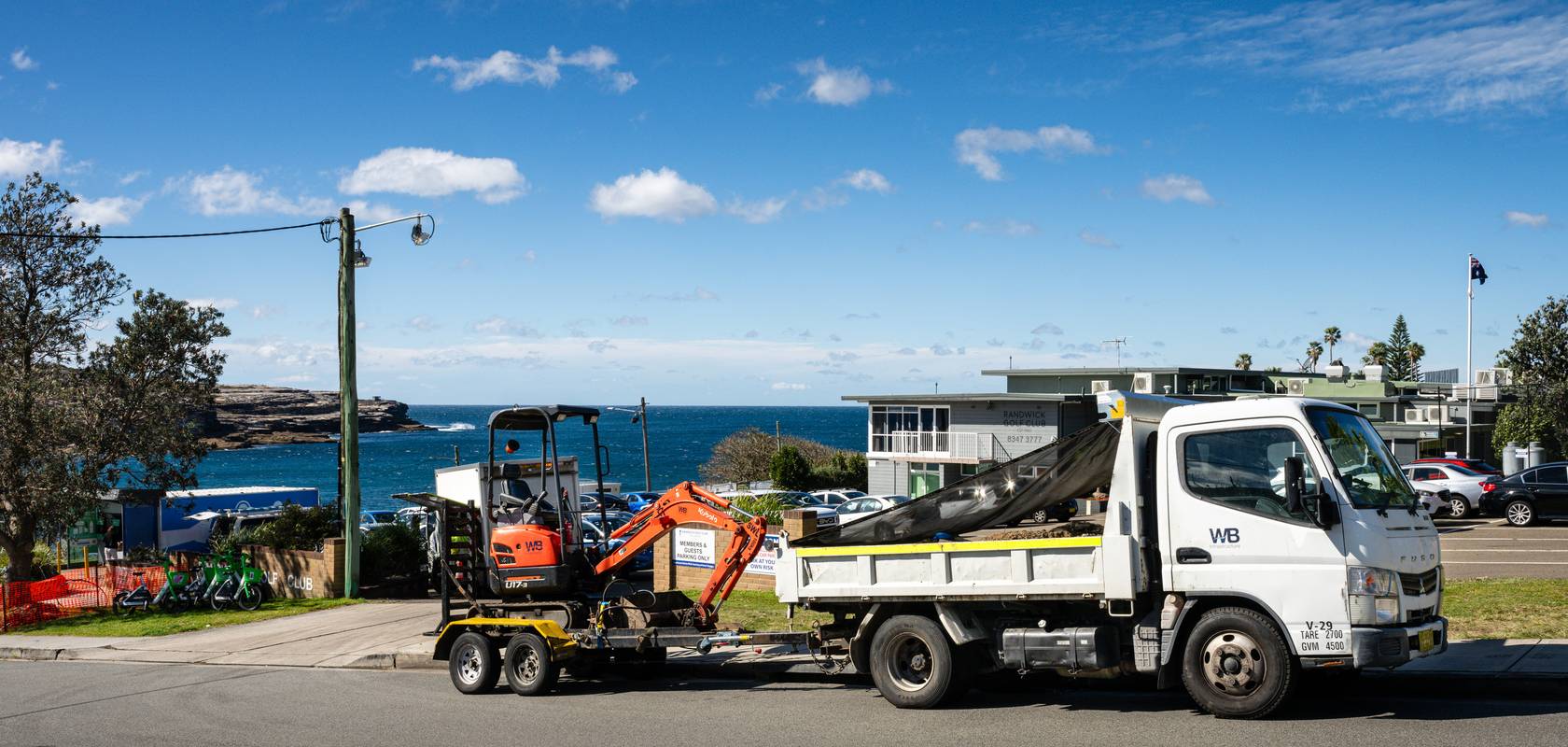 A WB truck carrying a mini excavator beside the coast.